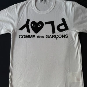 Vit Comme des Garçons Play t-shirt - Ny oanvänd Vit t-shirt från Comme des Garçons Play storlek S med svart tryck framtill. Ikoniskt hjärta med ögon och stor logga. Klassisk rund hals och korta ärmar. Skön och mjuk bomull, perfekt för en clean och stilren look. Köptes för 1500kr. Säljer för 549kr, Äkta vara