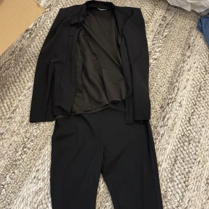 Svart kostymset  - Snyggt svart kostymset från SHEIN i storlek XS. Setet består av en ärmlös kavaj med enkel krage och matchande byxor med smal passform. 