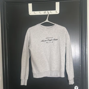 Grå sweatshirt Maison Degli Artisti XS - Gråmelerad sweatshirt från H&M i storlek XS med svart tryck på bröstet där det står 'Maison Degli Artisti'. Tröjan har rund halsringning, långa ärmar och ribbade muddar vid ärmslut och nederkant. Perfekt till hösten!