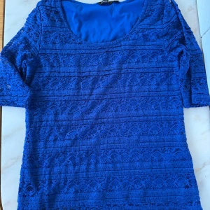Blå spetsblus med trekvartsärm - Snygg blå blus med vackert spetsmönster och rund halsringning. Blusen har trekvartsärmar och är helfodrad för en bekväm känsla. Perfekt för dig som vill sticka ut med färg och detaljer.