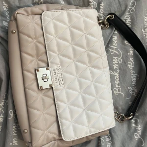 Quiltad axelväska från Guess - Snygg quiltad axelväska från Guess i beige och vitt med svart axelrem. Lite smutsig inne men inget man tänker på, skriv vid frågor och ge gärna prisförslag 