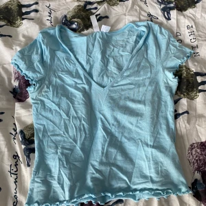 Ljusblå v-ringad topp med volangkant - Supersöt ljusblå topp med v-ringning och korta ärmar. Volangdetaljer vid ärmslut och nederkant ger en extra touch. Perfekt för dig som gillar en enkel men ändå söt stil.