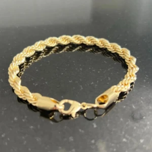 Flätat guldarmband med karbinlås - Snyggt armband i guldton med flätad design och robust karbinlås. Armbandet har en klassisk och stilren look som passar perfekt till din vardagsstil. Metallens glans ger en lyxig känsla och den tvinnade formen gör det extra unikt.