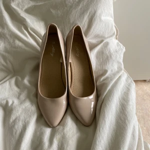Beige pumps med spetsig tå från Alley - Snygga beige pumps från Alley med spetsig tå och låg klack. Skorna har en glansig finish och är tillverkade i syntetmaterial. Perfekta för dig som gillar stilrena och klassiska vibes. Använt dom fåtal gånger.