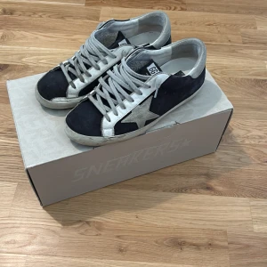 Golden Goose svarta och vita sneakers - Golden Goose sneakers med svart mocka, vita skinnpaneler och den ikoniska stjärnan i grå mocka på sidan. Storlek 40.