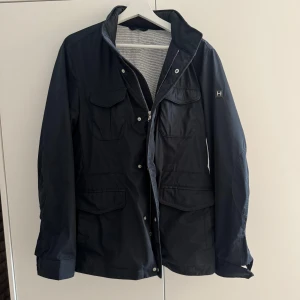 Hackett allvädersjacka - Säljer här en snygg mörkblå allvädersjacka från Hackett London, i storlek S. Nypris ca 5000kr. Mitt pris 800kr. En knapp har lossnat och någon fläck inuti men som lätt kan tvättas bort.