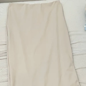 Beige långkjol i enkel stil - En stilren beige långkjol med rak passform. Kjolen har minimalistisk design utan synliga detaljer eller mönster, vilket gör den lätt att matcha med olika toppar. Perfekt för dig som gillar en clean och klassisk look.