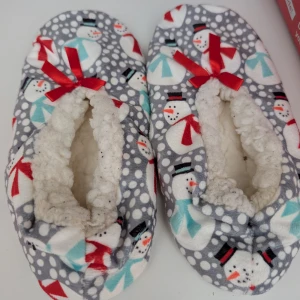 Grå tofflor med snögubbar och rosett - Mysiga grå tofflor med snögubbemönster, vita prickar och röda rosetter framtill. Insidan är fodrad med mjuk, vit fleece som håller fötterna varma. Perfekta för vintern och julen, med halkskydd under tofflorna men har inga sulor. Passar mig som har storlek 36-37 i skor 