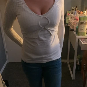 Vit ribbad kofta med cut-out detalj - Säljer en vit ribbad kofta med lång ärm och snygg cut-out detalj framtill. Koftan har två knappar vid bysten och är figurnära i modellen. Perfekt att styla över ett linne eller topp för en trendig look.