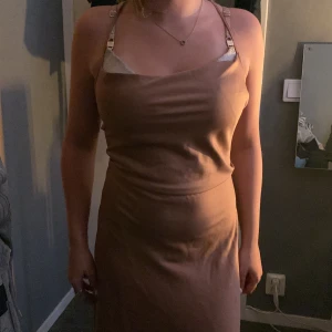 Champagnefärgad omlottklänning BikBok - Champagnefärgad midiklänning från BikBok i glansigt satinliknande material. Klänningen har smala axelband, öppen rygg med snörning och omlottdetalj baktill. Snygg och stilren passform som sitter figurnära men ändå bekvämt.