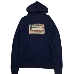 Mörkblå hoodie från Ralph Lauren - Snygg mörkblå hoodie från Ralph Lauren med amerikansk flagga och logga på bröstet. Klassisk känguruficka och huva, perfekt för en avslappnad streetstyle. Mjuk bomullskänsla och långa ärmar. Storlek xs, passar S bäst.