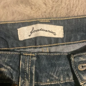 Blå jeans från Stradivarius - Säljer ett par blå jeans från Stradivarius med snyggt slitna detaljer och kontrastsömmar. Jeansen har klassisk femficksdesign, raka ben och coola broderier på bakfickorna. Perfekta för en avslappnad och trendig look.
