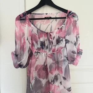 Blommig blus  - Supersöt kortarmad blus från Clara med stora blommönster. Lätt och luftig med transparenta ärmar, knytning vid halsen! 🩷🌸💕