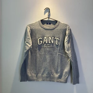 Grå sweatshirt från GANT - Snygg grå sweatshirt från GANT med broderad logga och text framtill. Klassisk rund halsringning och långa ärmar. Tröjan är i mjuk bomull och har ribbade muddar vid ärmslut och nederkant. Perfekt för en chill och stilren look.