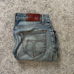 Ljusblå jeans från Tiger of Sweden - Snygga ljusblå jeans från Tiger of Sweden med klassisk femficksdesign och orangea sömmar. Jeansen har en rak passform och är tillverkade i mjukt denimtyg. Perfekta för en avslappnad och stilren look.