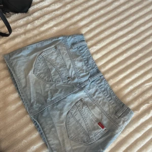 Ljusblå jeanskjol från ONLY - Snygg ljusblå jeanskjol från ONLY med klassiska fickor både fram och bak, bälteshällor och knappstängning. Perfekt för dig som gillar en enkel och tidlös look. Kjolen har raka linjer och en kort passform som ger en fräsch vibe.