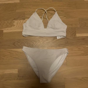 Vit ribbad bikini från H&M - Snygg vit bikini från H&M i storlek 38. Bikinin har ribbad struktur och består av en trekants-bh med smala axelband och matchande trosor. Perfekt för stranden eller poolen, enkel och stilren design som alltid funkar.