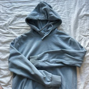 Ljusblå hoodie  - En stilren ljusblå hoodie från Divided med huva och snörning. Tröjan är i mjuk bomullsmix och har långa ärmar samt ribbade muddar. Perfekt för en chill och avslappnad look. Säljer för den inte kommer till användning. Köpt på Hm och passar både killar och tjejer. 