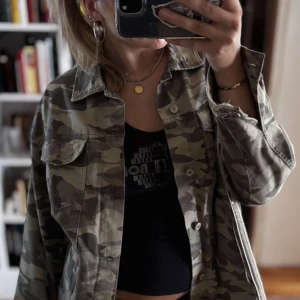 Camouflage jeansjacka från Zara - Säljer en snygg camouflagefärgad jeansjacka från Zara Z1975 Denim. Jackan har klassisk krage, knäppning framtill och två bröstfickor. Tillverkad i bomull, perfekt för dig som vill sticka ut med en cool streetstyle-look.