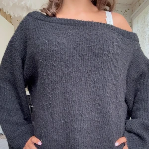 Svart stickad offshoulder-tröja - Mysig svart stickad tröja med offshoulder-design och lång ärm. Tröjan har en loose passform och bred halsringning som ger en avslappnad vibe. Perfekt för kyliga dagar när du vill vara både bekväm och snygg.