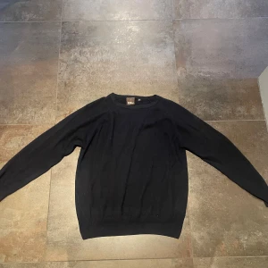 Mörkblå stickad tröja från  Oscar Jacobson - En klassisk marinblå stickad tröja från Oscar Jacobson. Tröjan har rund halsringning och långa ärmar, perfekt för lager-på-lager. Tillverkad i Italien och känns riktigt mjuk och skön mot huden. Enkel och stilren design som funkar till det mesta.