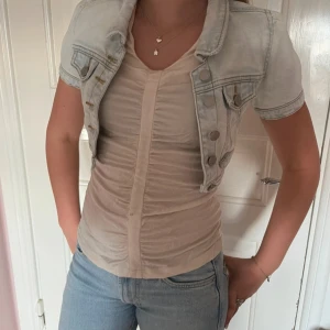 Ljusblå croppad jeansjacka - Säljer en ljusblå croppad jeansjacka med korta ärmar och snygga silvriga knappar. Jackan har klassiska bröstfickor och en cool, avslappnad vibe. Perfekt att slänga över en topp för en trendig look.