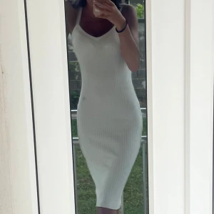 Vit ribbad ärmlös klänning - Säljer en vit, ribbad klänning med smala axelband och figurnära passform. Klänningen är midilång och har en enkel, stilren design som passar perfekt till varma dagar. Materialet är stretchigt och bekvämt.