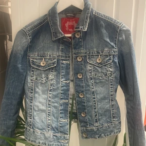 Klassisk blå jeansjacka från edc - Snygg blå jeansjacka från edc med coola slitningar och kontrastsömmar som ger en vintage look. Jackan har knappar framtill, två bröstfickor med lock och lång ärm. 