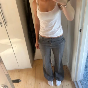 Grå lågmidjade kostymbyxor bootcut - Snygga grå kostymbyxor med låg midja och bootcut-ben. Byxorna har klassiska fickor fram och bak, bälteshällor och stängs med dragkedja och knapp. Perfekta för en clean och stilren look. Byxorna är aldrig använda. Köpt för 400