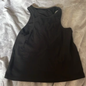 Svart ribbad linnetopp - En svart ribbad linnetopp med breda axelband och rundad halsringning. Toppen är ärmlös och har en enkel, stilren design som passar perfekt till jeans eller kjol. Materialet är mjukt och stretchigt för en bekväm känsla.