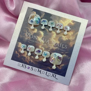 ShellBaby 🐚 (S); Square Toes - Handgjorda toe press-on naglar i S: 14 mm, 9 mm, 9,5 mm, 9 mm, 6 mm, med skimrande vit bas, dekorerade med holografiska snäckskal, stjärnor och fjäderdetaljer i blått, lila och rosa. Naglarna har en kvadratisk form och ger en unik, havsinspirerad look. Perfekt för dig som vill sticka ut med kreativa tånaglar.