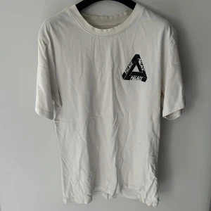 Vit Palace t-shirt med stor logga - Vit t-shirt från Palace med ikonisk Tri-Ferg-logga i svart, gult och grönt på ryggen och mindre logga på bröstet. 