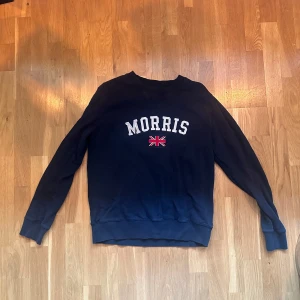 Mörkblå sweatshirt från Morris - Snygg mörkblå sweatshirt från Morris med vit broderad logga och brittisk flagga framtill. Klassisk rund halsringning och långa ärmar.