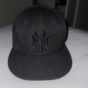 Svart fitted New Era Yankees keps - Snygg svart New Era keps med New York Yankees-logga broderad framtill i svart. Klassisk modell med böjd skärm och broderade ventilationshål. Kepsen är helsvart och har diskreta loggor på sidan och bak. Perfekt för dig som gillar stilrena accessoarer.