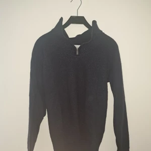 Mörkblå stickad half zip tröja - Mysig mörkblå stickad tröja med half zip och hög krage. Perfekt för kyliga dagar och enkel att matcha med jeans eller byxor. Långärmad modell med ribbade muddar för extra komfort och stil.