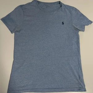Blå t-shirt från Polo Ralph Lauren - Snygg ljusblå t-shirt från Polo Ralph Lauren i custom fit. Klassisk design med korta ärmar och rund hals. Liten broderad logga på bröstet. Perfekt för en chill och stilren look. Har ett jättelitet hål som om en nål gått igenom så man märker inte alls. Storlek S