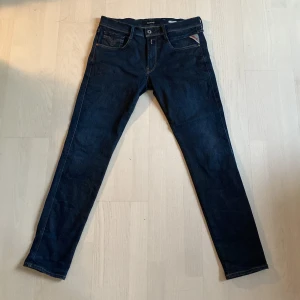 Mörkblå Replay Anbass jeans strl 34/32 - Snygga mörkblå jeans från Replay, modell Anbass. Klassisk femficksdesign med kontrastsömmar och läderpatch bak i midjan. Jeansen har en slim passform och raka ben, tillverkade i stretchig denim för extra komfort.