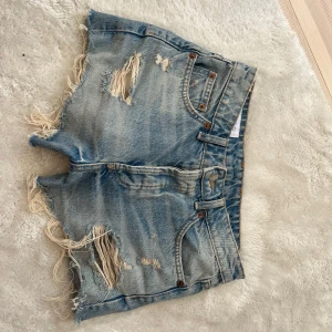 Blå slitna jeansshorts från Zara - Snygga blå jeansshorts från Zara med slitna detaljer och fransiga kanter. Klassisk femficksmodell med medelhög midja och råa benslut. Perfekta för sommaren när du vill ha en avslappnad och trendig look.