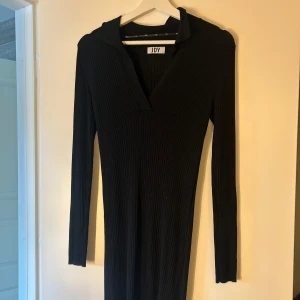 Svart ribbad klänning från JDY - Svart ribbad klänning från JDY med lång ärm och v-ringad krage. Klänningen är figurnära och har en klassisk, stilren look som passar perfekt till sneakers eller boots. Materialet är stretchigt och bekvämt, vilket gör den enkel att bära hela dagen.❤️