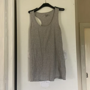 Grå linnetopp från Basic You - Säljer en enkel och stilren grå linnetopp från Basic You i ekologisk bomull. Modellen är ärmlös med klassisk racerback och rund halsringning. Perfekt för en avslappnad look eller till träning. Supermjuk och lätt att matcha med allt.