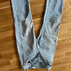 Ljusblå raka jeans från Zara - Säljer ett par ljusblå jeans från Zara med klassisk femficksdesign och raka ben. Jeansen har knäppning med knappar framtill och är tillverkade i bomull. Perfekta för en avslappnad och trendig look.