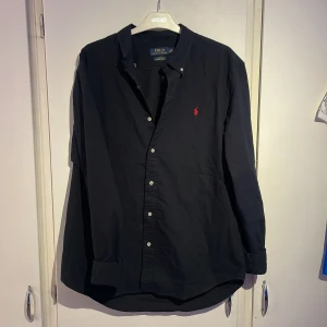 Navy skjorta Polo Ralph Lauren  - Svart långärmad skjorta från Polo Ralph Lauren i slim fit stretch oxford. Klassisk skjortkrage, knäppning framtill och ikonisk röd broderad logga på bröstet. Skjortan är i bomull och har en stilren, tidlös look som passar till många olika outfits. Storlek XL sitter som L. Priset är ej hugget i sten✌🏽