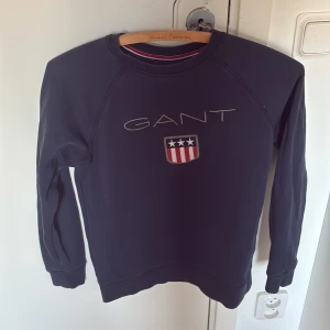Mörkblå Gant tröja - Stilren Gant-tröja med tryck och text där fram på. Skönt material och lätt att styla. Storleken är 158/164. Skriv om du har frågor😊