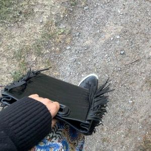 Svart kuvertväska med fransar ifrån maje  - Säljer en svart maje väska  i croco-mönstrat skinn med coola fransdetaljer på sidorna. Väskan har en stilren och edgy look, perfekt för att lyfta vilken outfit som helst. Liten och smidig att bära med sig.