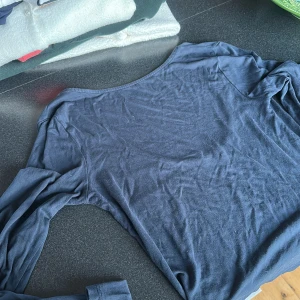 Mörkblå långärmad topp med rund hals - En basic mörkblå långärmad topp i mjuk bomull med rundad, lite djupare halsringning. Perfekt att styla med jeans eller kjol för en clean look. Enkel och stilren design utan tryck eller mönster.