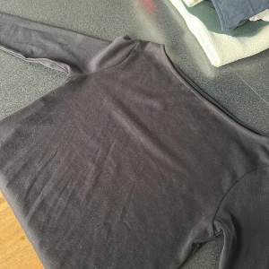 Svart långärmad topp från 157 - En svart långärmad topp från 157 i mjuk och stretchig bomullsblandning. Enkel och stilren design med rund halsringning, perfekt att matcha med jeans eller kjol. Materialet är 94% bomull och 6% elastan för en skön passform.