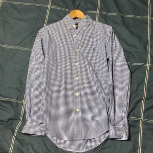 Blårutig Ralph Lauren skjorta  - Blårutig skjorta från Ralph Lauren i slim fit-modell. Skjortan har klassisk krage, knäppning framtill och lång ärm. Broderad grön logga på bröstet.