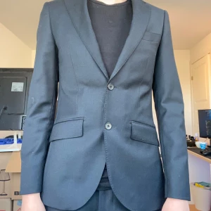 Svart kostym med kavaj och byxor - Stilren svart kostym med tvåknäppt kavaj och matchande byxor. Jätte bra skick och har använts 1-2 gånger. Modellen är 175 cm och 65 kg. Säljer för att den är liten. 