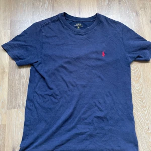 Marinblå t-shirt från Polo Ralph Lauren - Snygg marinblå t-shirt från Polo Ralph Lauren. Tröjan är storlek M men passar mer S/XS pga slim fit passformen. Tröjan har även en pytteliten defekt som knappt syns. 