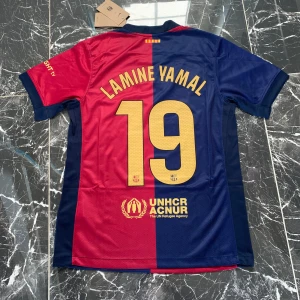 FC Barcelona Lamine Yamal matchtröja - Säljer en officiell FC Barcelona matchtröja från Nike med Lamine Yamal och nummer 19 på ryggen. Tröjan har klassisk halvblå, halvröd design med gula detaljer och klubbmärke på bröstet. Tillverkad i lätt och ventilerande polyester, perfekt för fotbollsplanen.